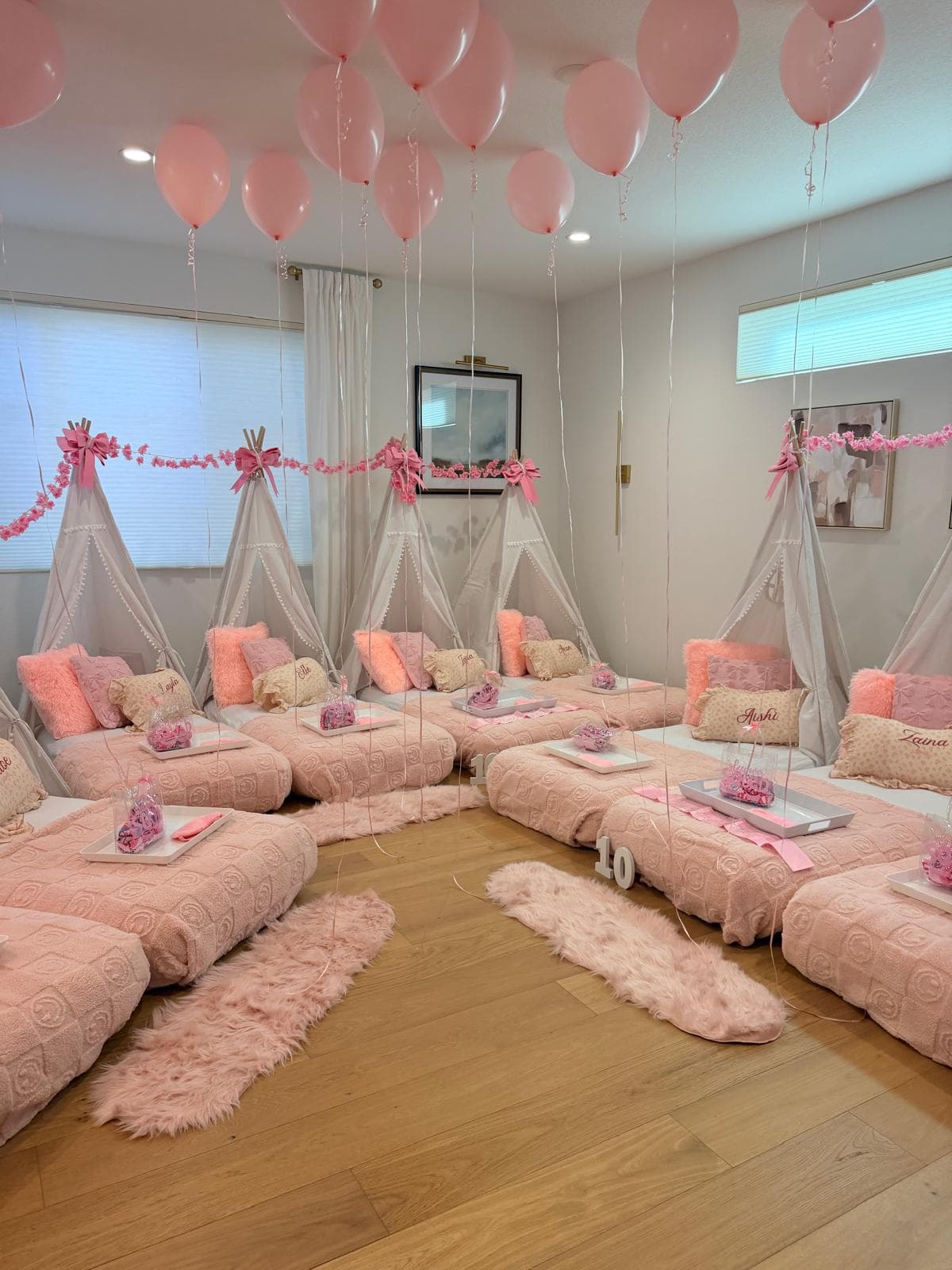 Slumber party room with pink balloons hanging over teepee beds and fluffy rugs