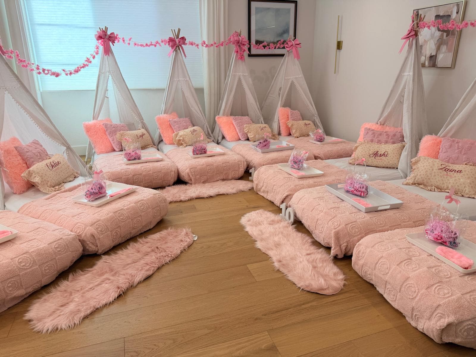 Pink teepee sleepover with floor beds, trays, and a floral garland in a bright room